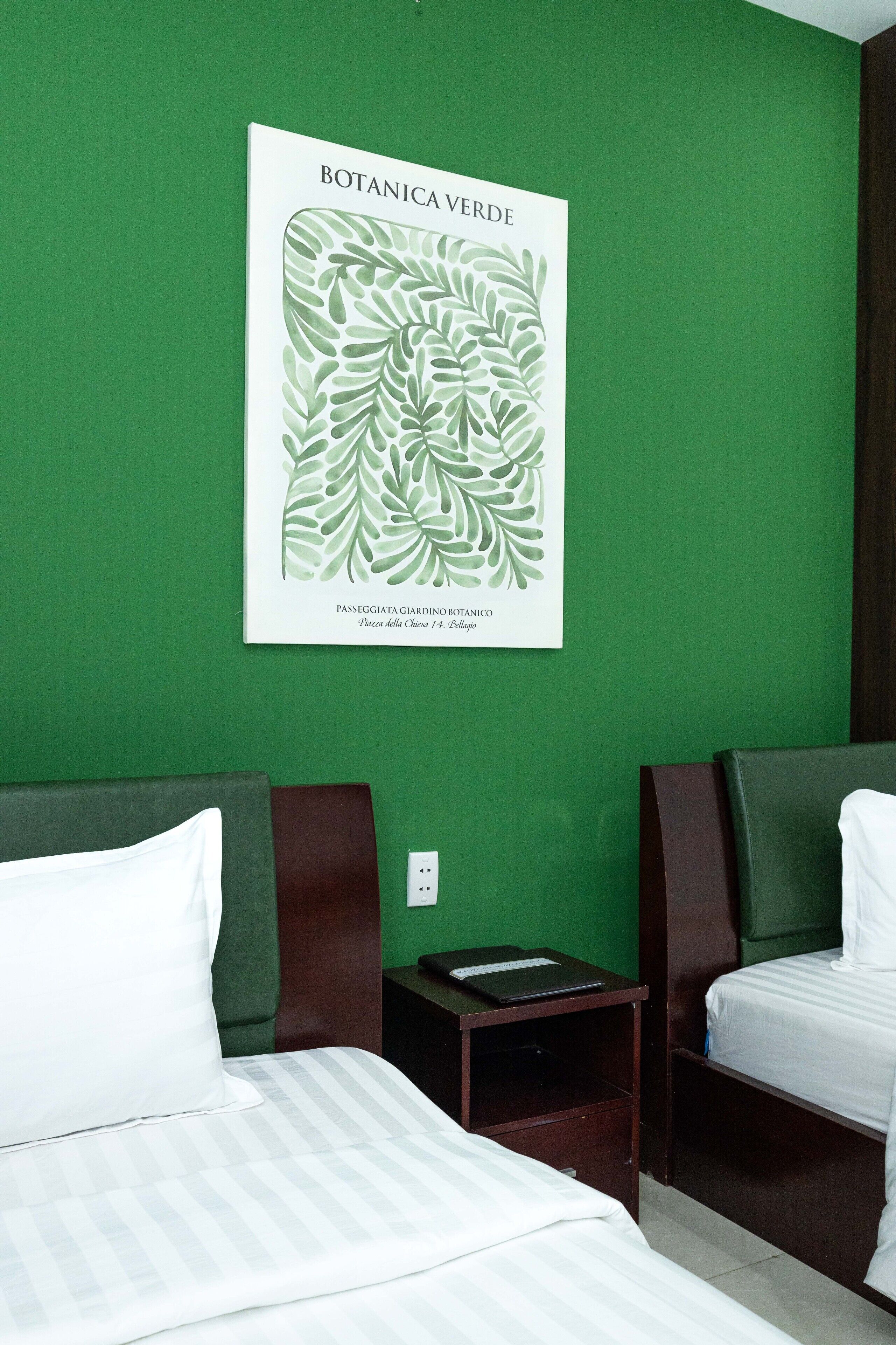 A hotel room with two beds, a green wall, and a botanical print.