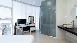 A modern hotel room with a large bed, a television, a minibar, a glass-enclosed shower, and a large window offering a city view. - Happy Home Boutique Hotel Vung Tau (Ho Chi Minh City)