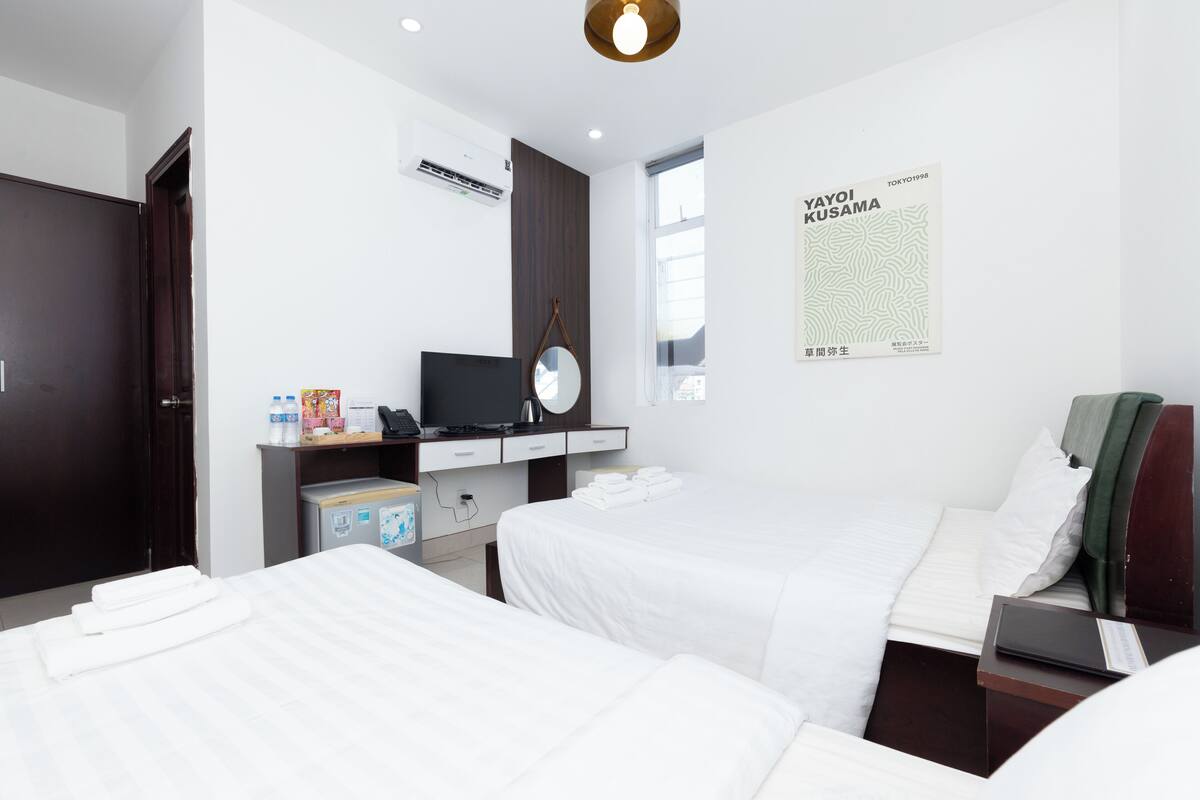 Ein Hotelzimmer mit zwei Betten, einem Schreibtisch mit Computer, einem Spiegel und einem Poster an der Wand.