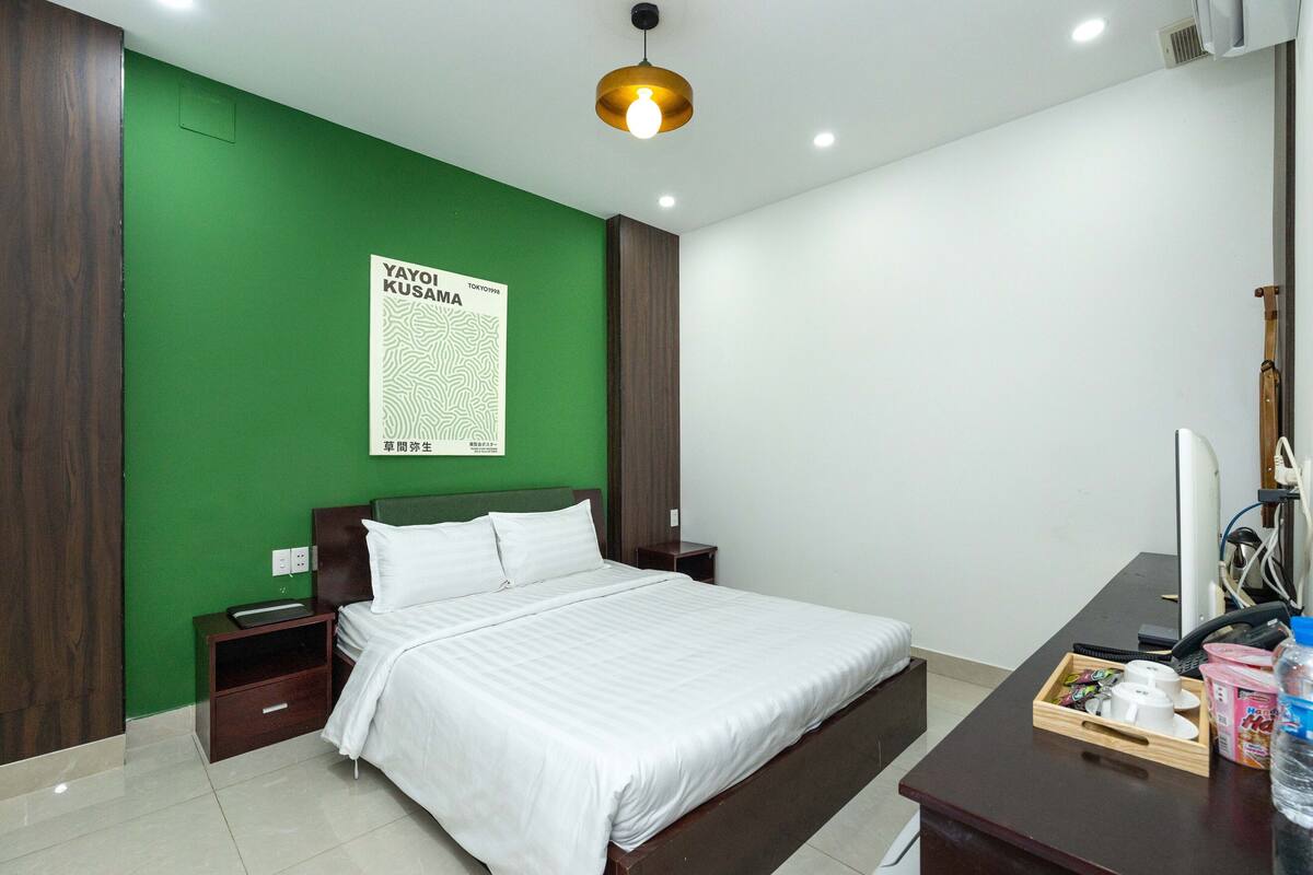 Ein Hotelzimmer mit einer grünen Akzentwand, einem Bett mit weißer Bettwäsche, einem Nachttisch aus Holz, einem Schreibtisch mit einem Computer und einem Poster an der Wand.