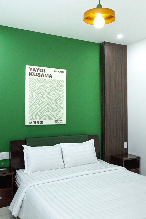 Una habitación de hotel con una pared verde, una cama con ropa de cama blanca, una mesita de noche, un armario de madera y un cartel en la pared.