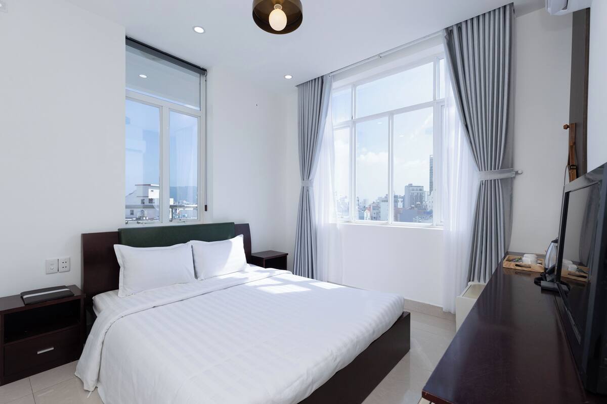 Ein modernes Hotelzimmer mit einem großen Bett, einem Schreibtisch und Blick auf die Stadt durch große Fenster.