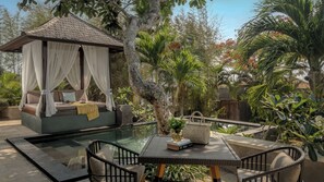 Un jardín privado con piscina cubierta por vidrio, una cama con dosel y mobiliario exterior.