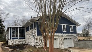 A two-story house with a stone facade, a garage, and a landscaped front yard with a tree.