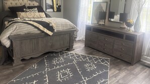A bedroom with a large bed, a dresser, a mirror, and a rug.