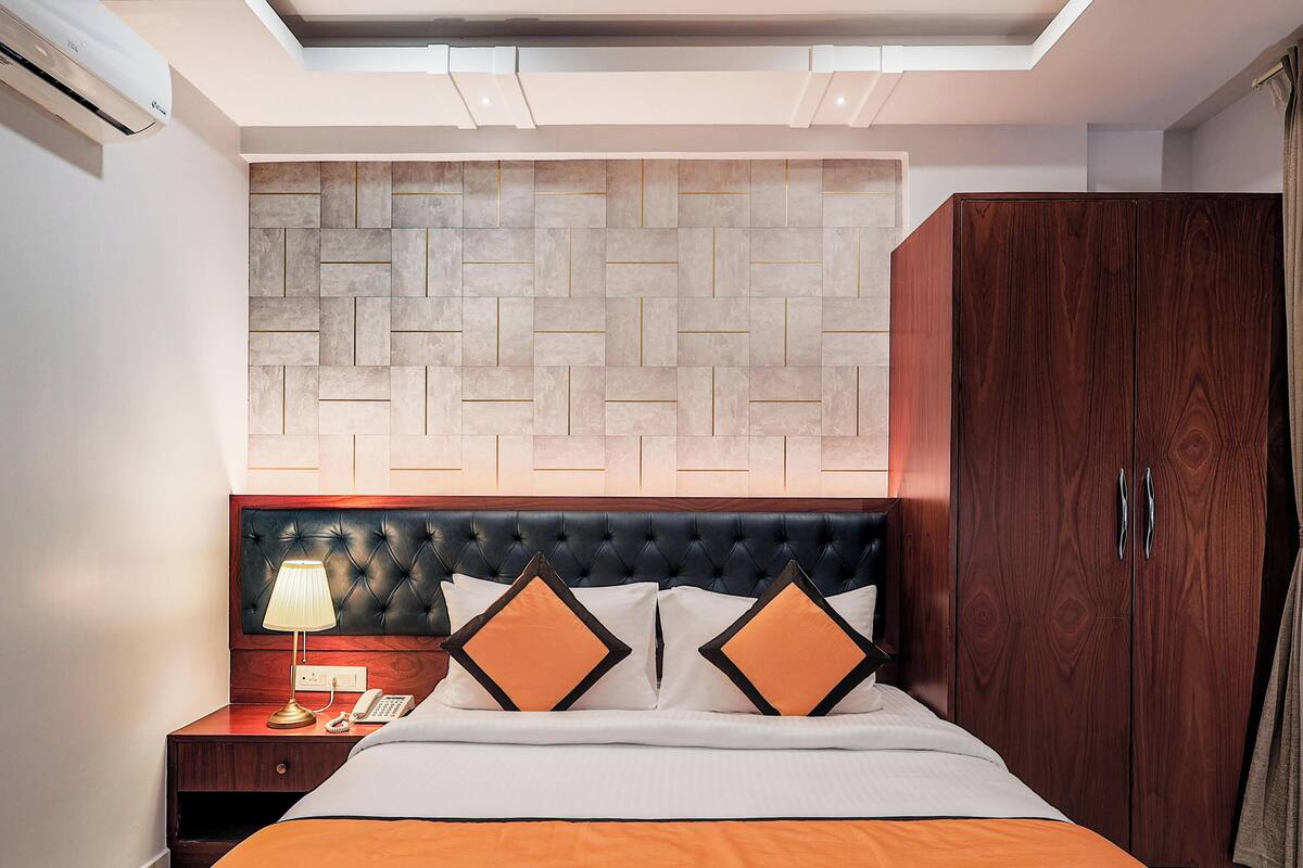 Una habitación de hotel con una cama, una mesita de noche, aire acondicionado, un armario y un cabecero con estampado de espiga.
