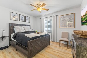 Ein Schlafzimmer mit Bett, Stuhl, Deckenventilator und einem Fenster mit Vorhängen.