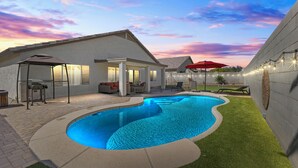 Ein Garten mit Schwimmbad, Terrassenmöbeln und einem überdachten Sitzbereich.