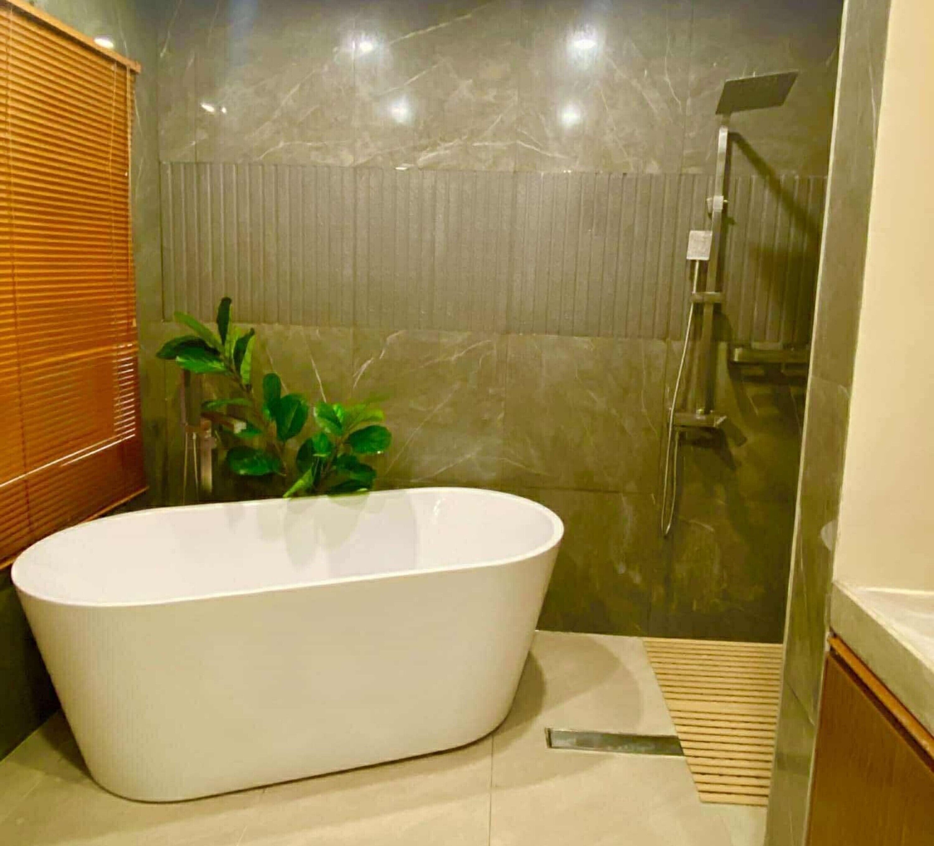 A modern bathroom with a freestanding bathtub, a shower area, and a potted plant.