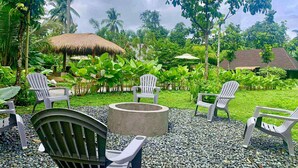 A tropical outdoor seating area with white plastic chairs and a concrete fire pit. - The Bali Farm (Liliw)