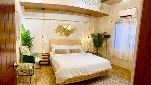 A modern bedroom with a wooden bed, a patterned rug, and two potted plants. - The Bali Farm (Liliw)