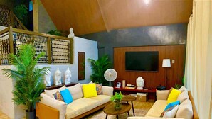 A living room with two sofas, a coffee table, and a TV. There are plants and decorative items on the shelves. - The Bali Farm (Liliw)