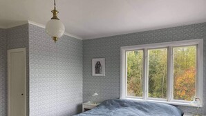 A bedroom with a bed, a nightstand, a lamp, a window with a view of trees, and patterned wallpaper. - 4 Star Holiday Home in Torsaker (Torsåker)