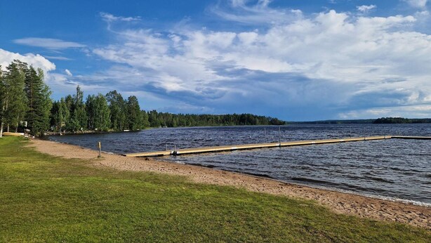 A lakeside view with a dock extending into the water, surrounded by grassy areas and dense trees. - 4 Star Holiday Home in Torsaker (Torsåker)