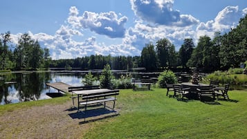 Un área de picnic junto al lago con bancos y mesas, rodeada de árboles y un cielo despejado.