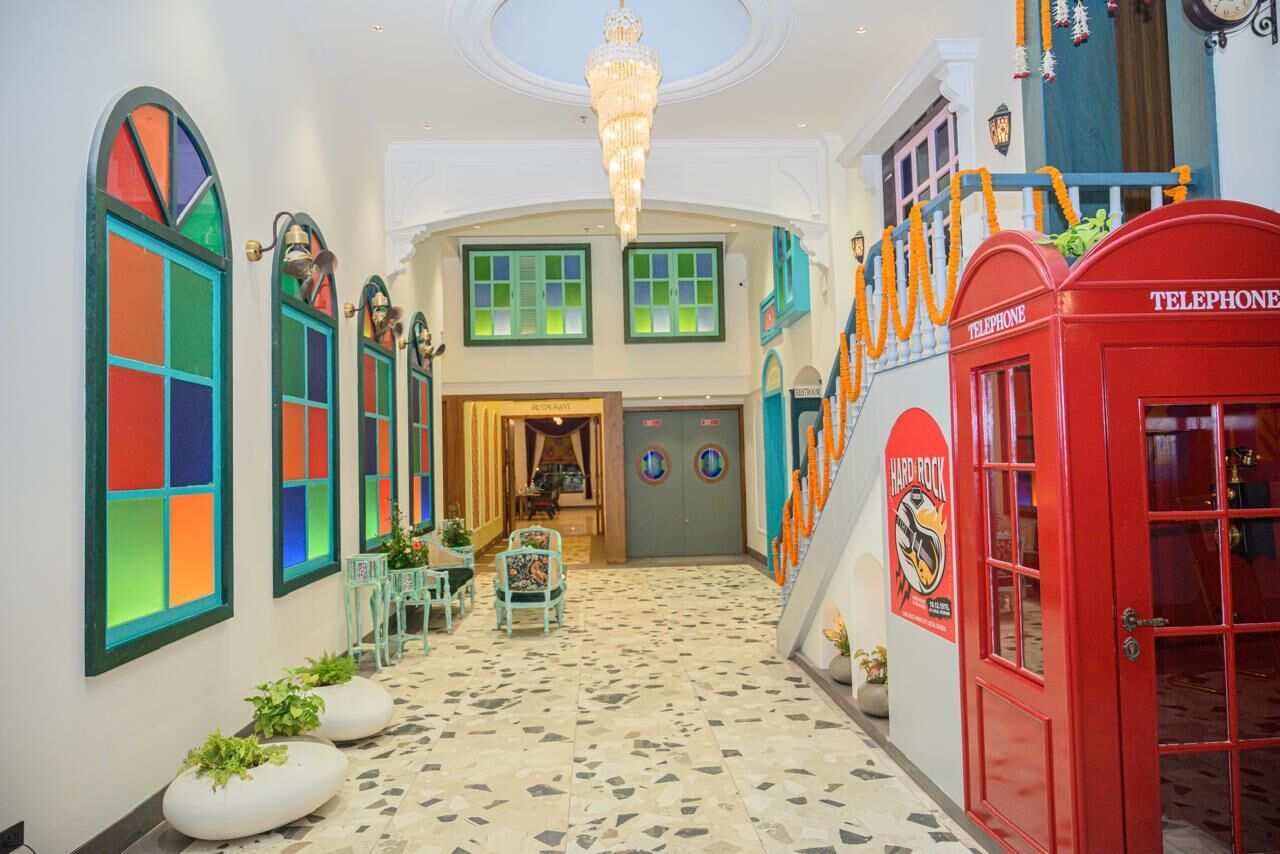 A hotel lobby with a central staircase, a red telephone booth, and colorful window designs.