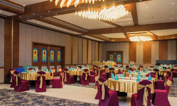 A banquet hall with round tables, chairs, and a chandelier.