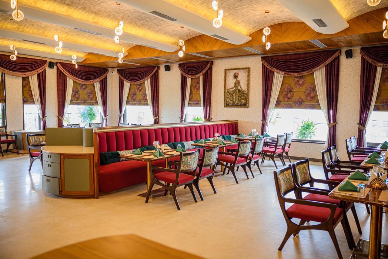 A restaurant with a central red booth seating area, individual tables with chairs, and a ceiling with exposed wooden beams and hanging lights.