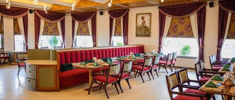 Un restaurante con una zona central de cabinas rojas, mesas individuales con sillas, y un techo con vigas de madera a la vista y luces colgantes.