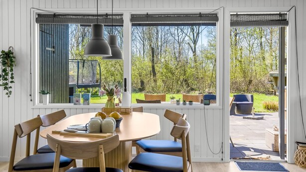 Un coin repas avec une table ronde, six chaises et une vue sur l’extérieur grâce à de grandes fenêtres.