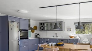 Une cuisine moderne avec des meubles gris, un réfrigérateur en acier inoxydable, une table à manger en bois avec des chaises et des luminaires suspendus.