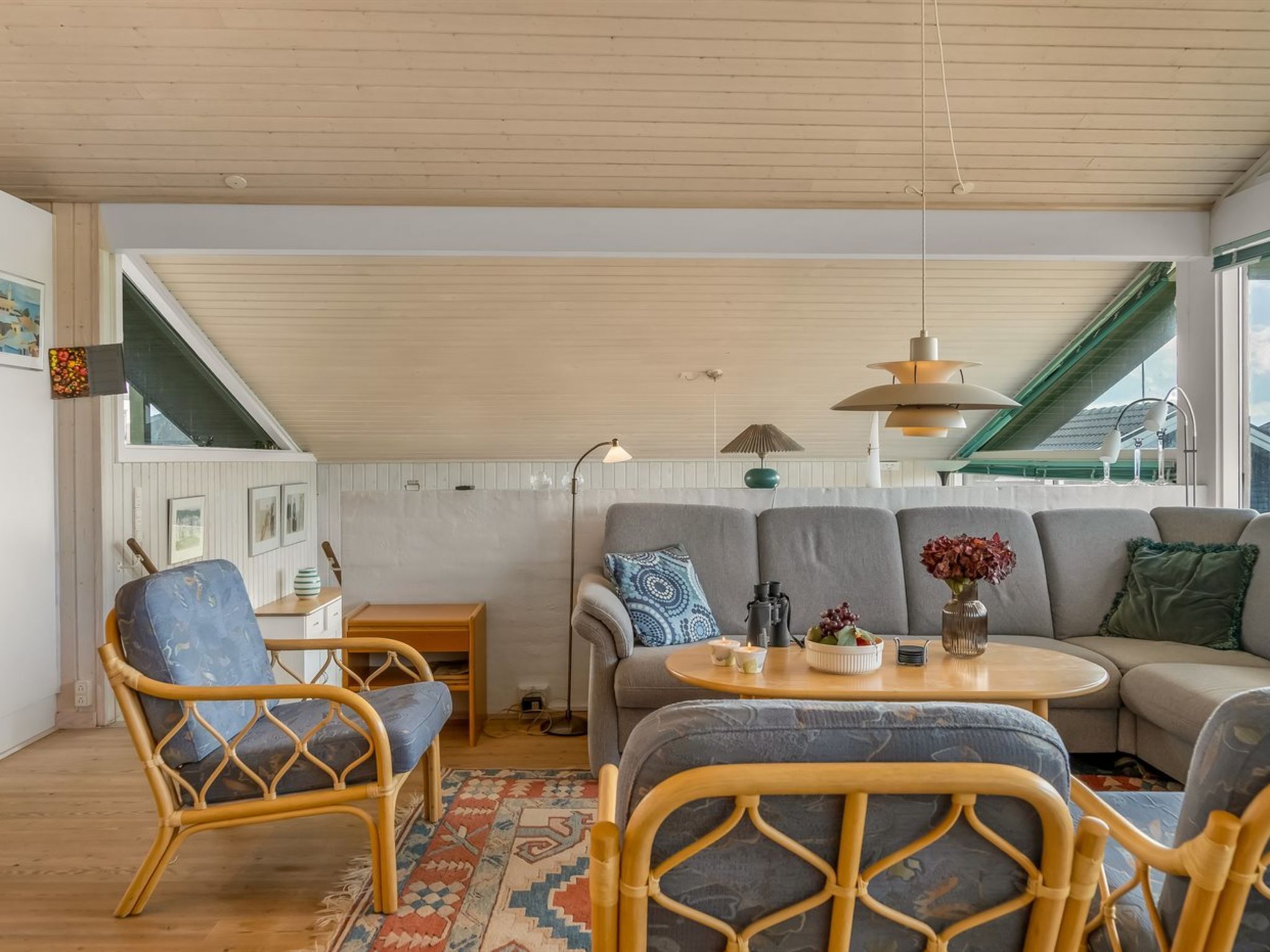 Uma sala de estar aconchegante com pé direito alto, um conjunto de sofás, uma mesa de jantar e cadeiras de vime.