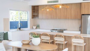 Una cocina moderna con armarios de madera, una isla central con taburetes de bar, una mesa de comedor e iluminación colgante.