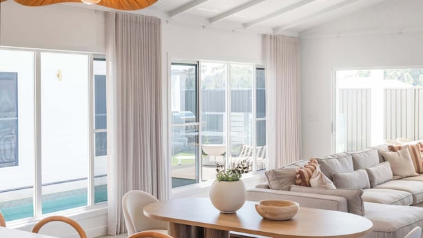 Una sala de estar moderna con un sofá grande, una mesa de comedor con sillas y ventanas amplias con cortinas.