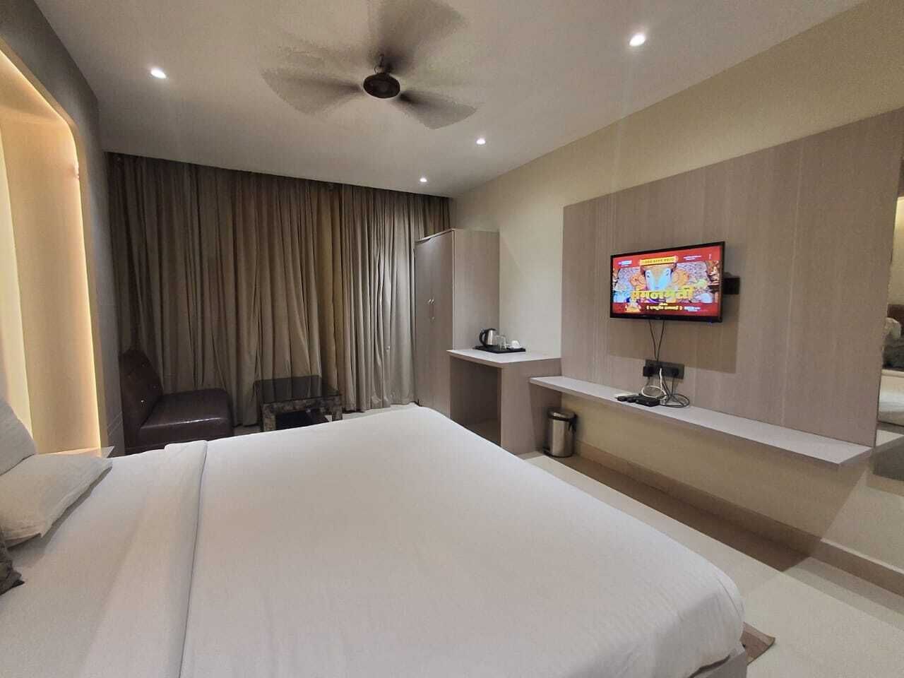 A modern hotel room with a large bed, a desk, a television, and a ceiling fan.