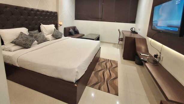 A modern hotel room with a large bed, a desk, a flat-screen TV, and a ceiling fan. - Hotel Downtown (Bilaspur)