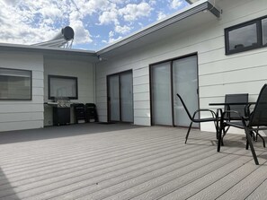 Une terrasse extérieure moderne, dotée d’une plateforme en bois, d’un barbecue et d’un coin repas avec des chaises en métal.