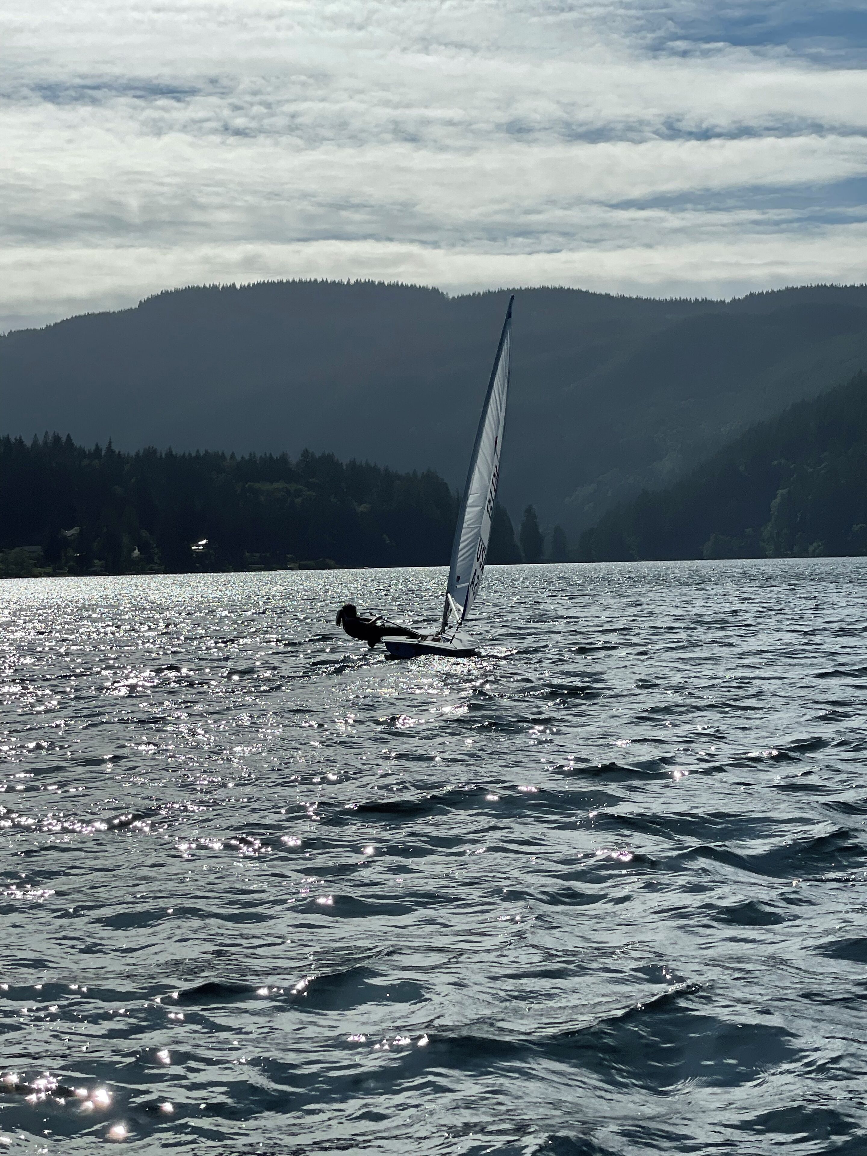 A sailboat on a calm lake with a forested mountain in the background.