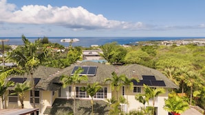 A house with solar panels, a swimming pool, and a view of the ocean and distant buildings. - Kona Nook - Cozy Studio with Island Warmth (Kailua-Kona)