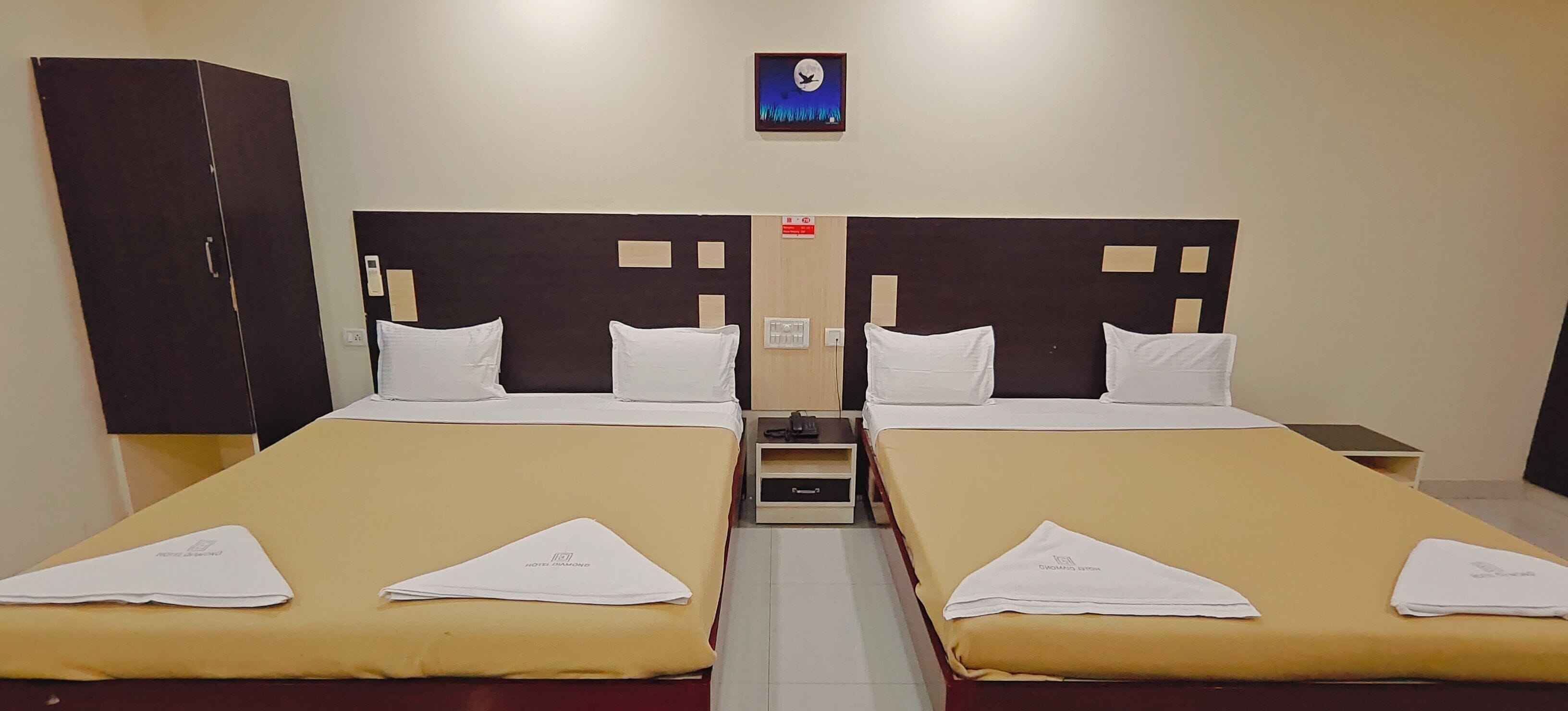 A hotel room with two single beds, a wardrobe, a nightstand, and a wall clock.