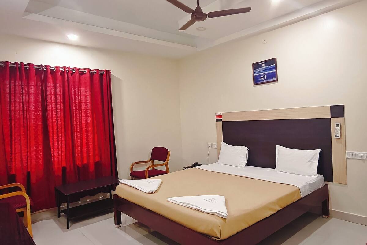 A hotel room with a bed, a desk, a chair, a red curtain, and a ceiling fan.