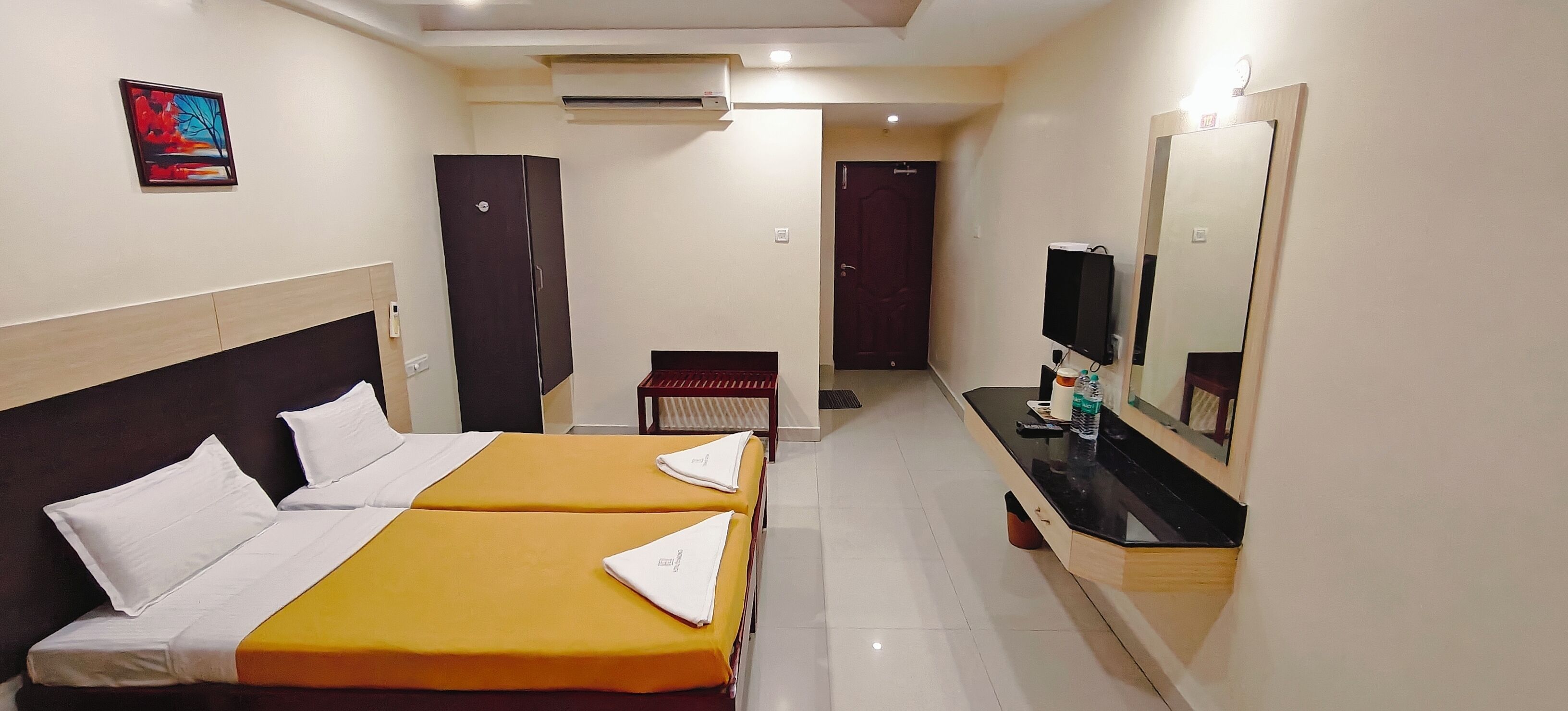 A hotel room with two beds, a desk, a TV, and an air conditioning unit.