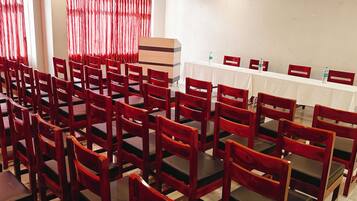 A conference room with rows of wooden chairs and tables, red curtains, and a whiteboard.
