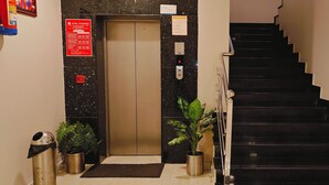 Um elevador com uma placa indicando uso exclusivo para hóspedes, uma escadaria com degraus pretos e duas plantas em vasos no chão.