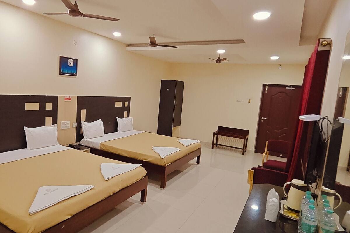 A hotel room with two single beds, a desk with a chair, a mirror, a ceiling fan, and a clock on the wall.
