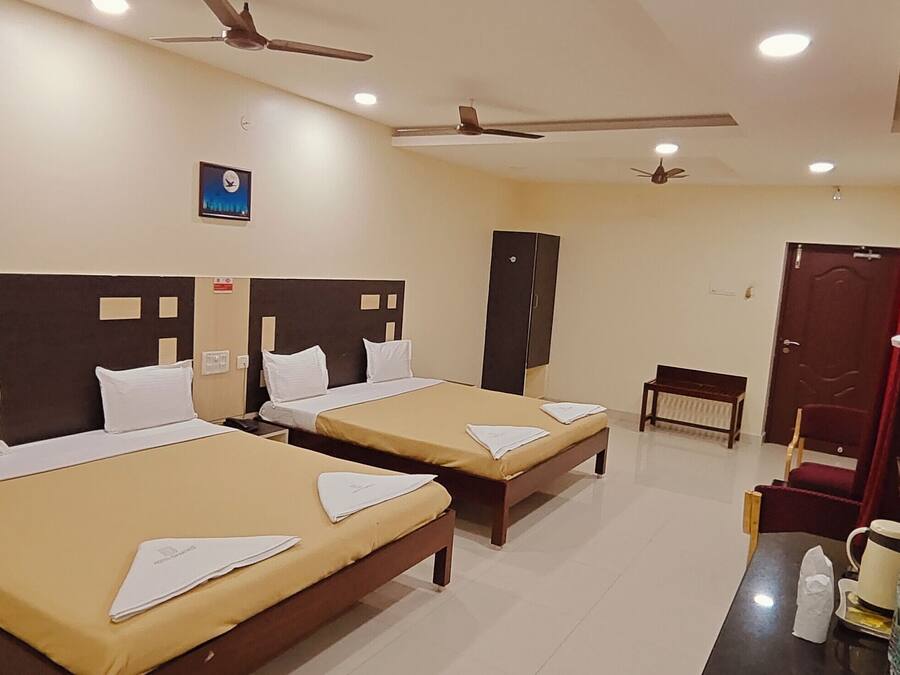 A hotel room with two single beds, a desk with a chair, a mirror, a ceiling fan, and a clock on the wall.