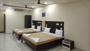 Quarto de hotel com duas camas, um guarda-roupa, um pequeno armário e um ventilador de teto.