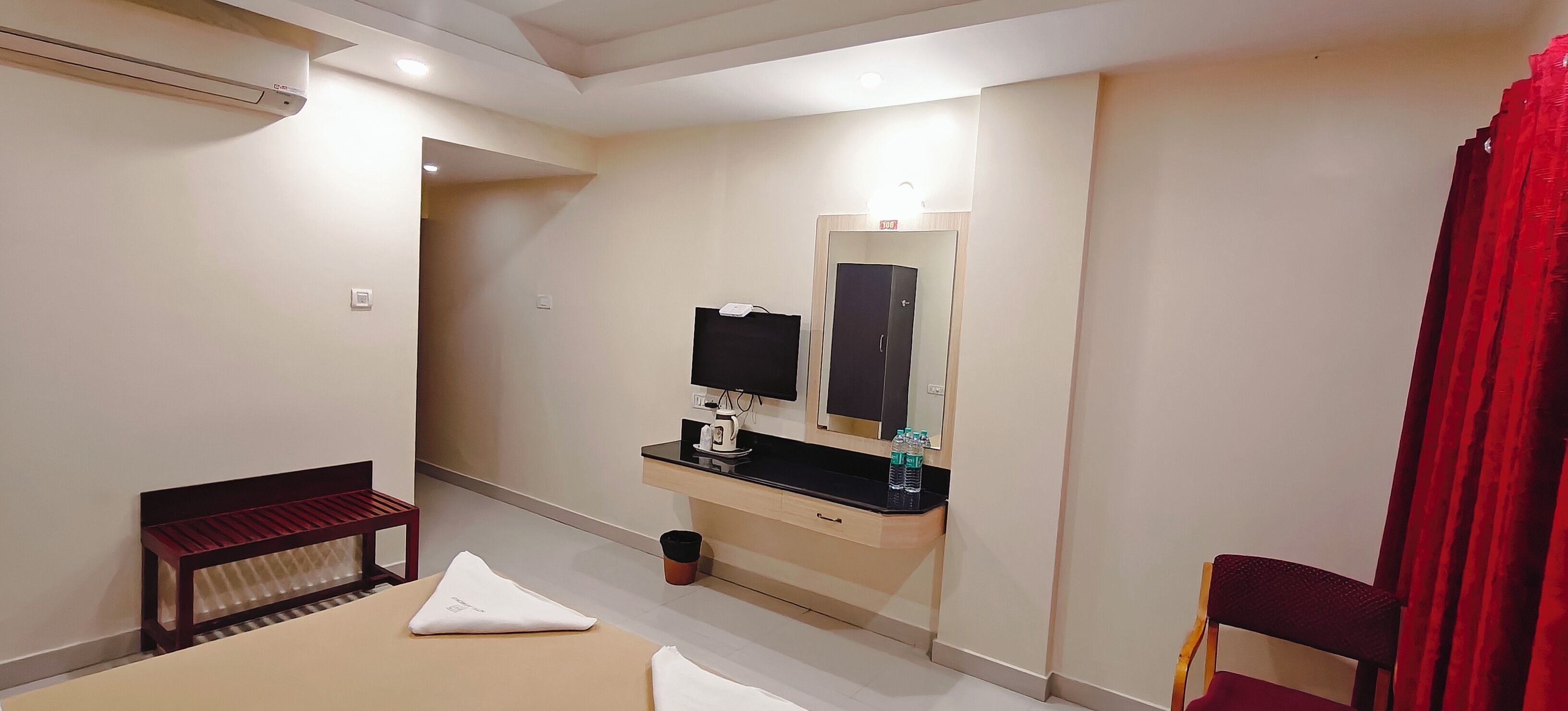 Ein Hotelzimmer mit Bett, Schreibtisch, Spiegel, Fernseher und einem roten Vorhang.