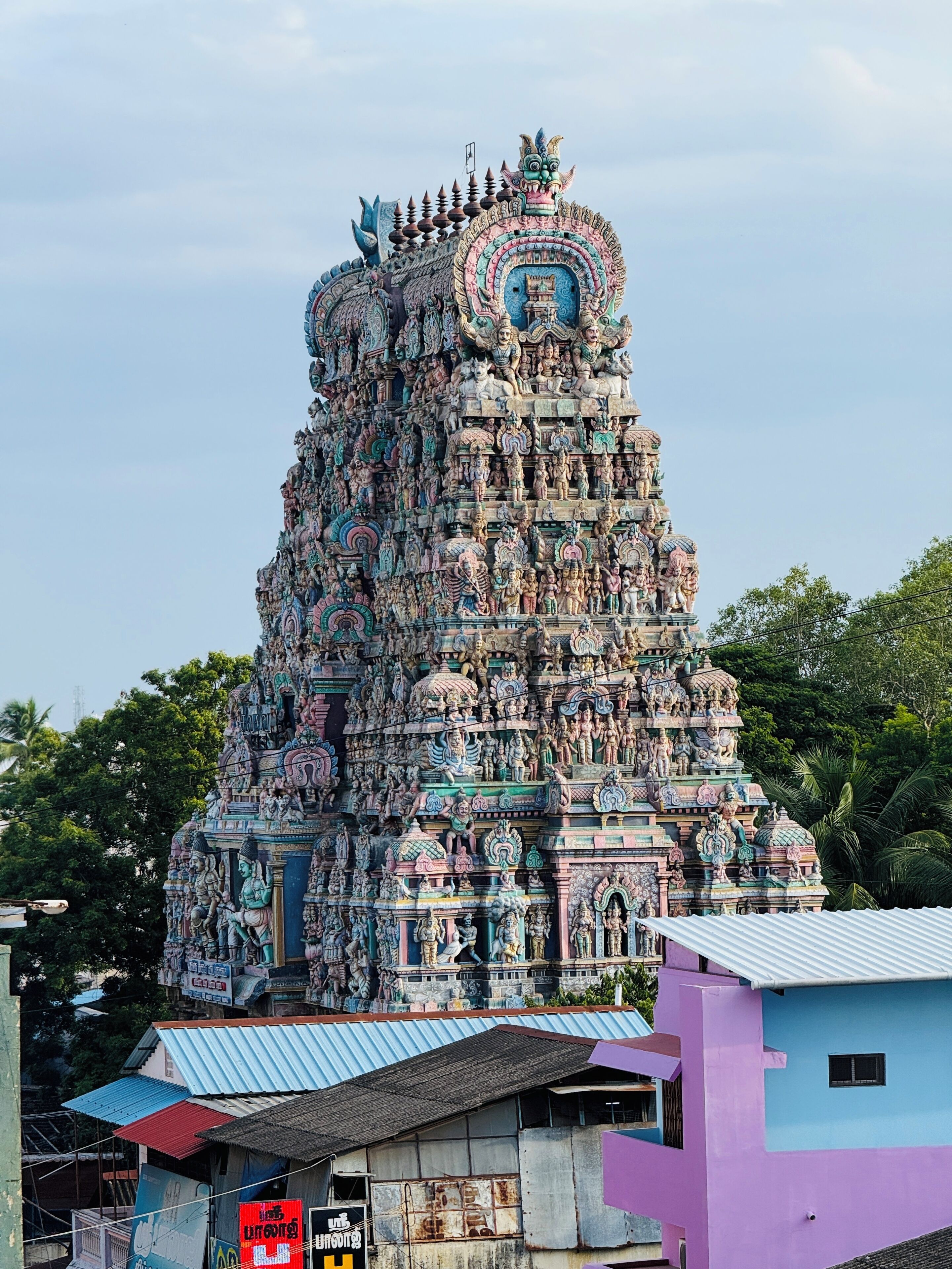 A multi-tiered temple with intricate carvings and statues, surrounded by residential buildings.