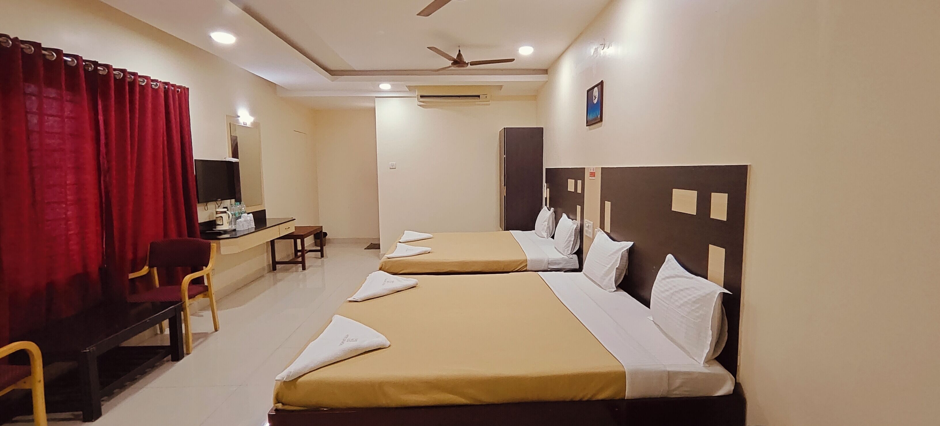 A hotel room with two beds, a desk, a chair, a television, and a ceiling fan.