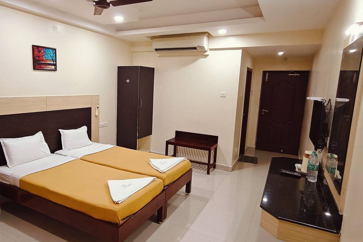 A hotel room with a double bed, bedside tables, a small desk, an air conditioning unit, and a mirror.