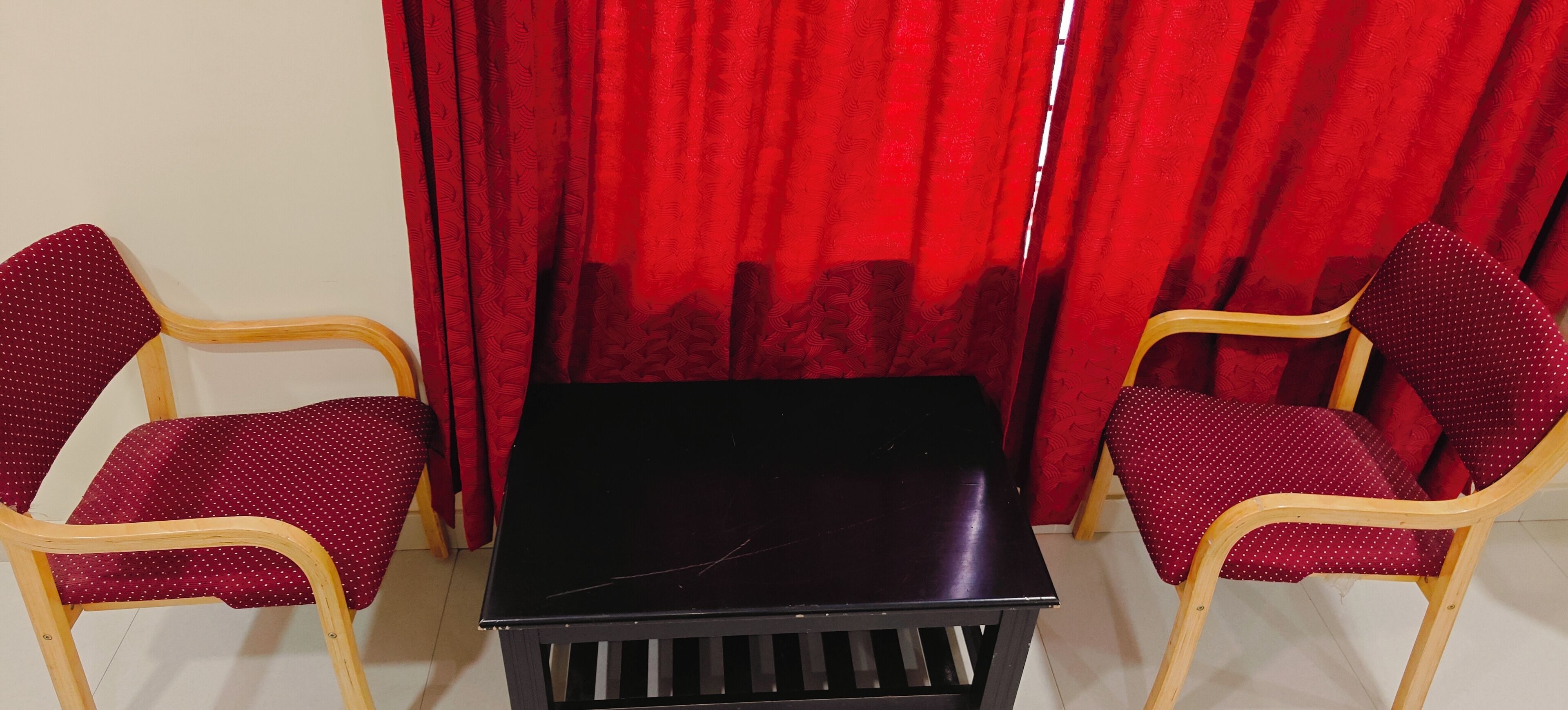 A room with two wooden chairs with red cushions, a black table, and red curtains.