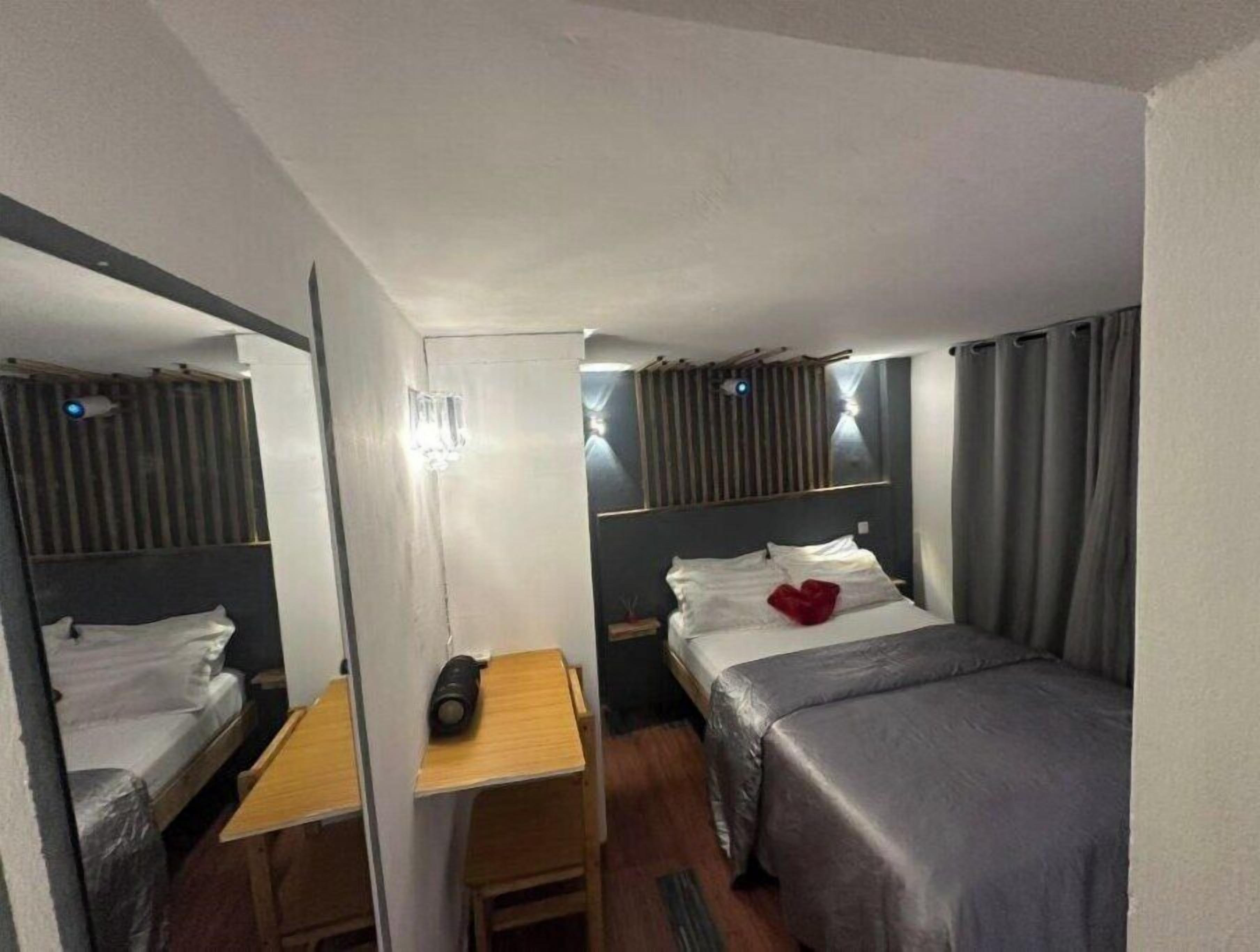 A hotel room with a bed, a desk, a chair, a mirror, and a nightstand.