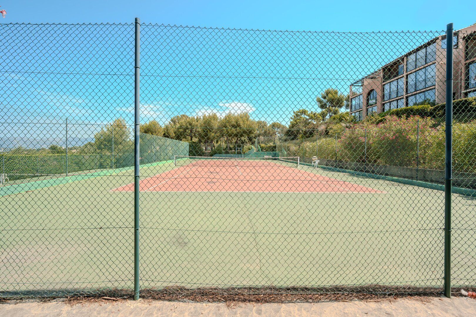 Un campo da tennis recintato con un edificio adiacente.