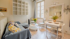Ein Zimmer mit einem Bett, einem Schreibtisch, einem Stuhl, einem kleinen Tisch mit Blumenvase und einem großen Spiegel.