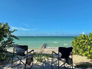 Uitzicht op een strand met twee stoelen gericht op de oceaan, een houten looppad en begroeiing.
